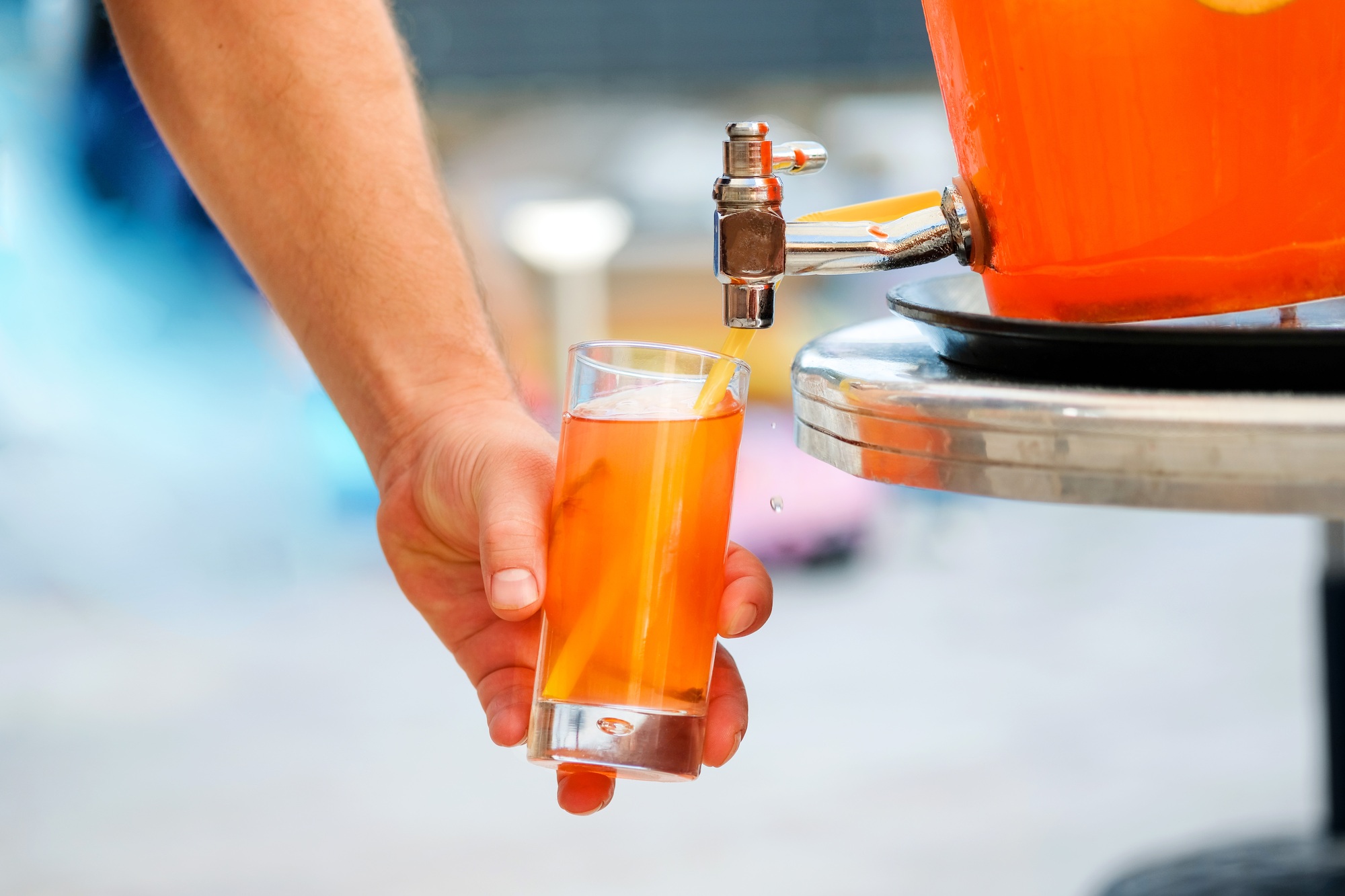 Man hand pouring fresh sorbet fruit juice or alcohol punch from drinking tank machine at party